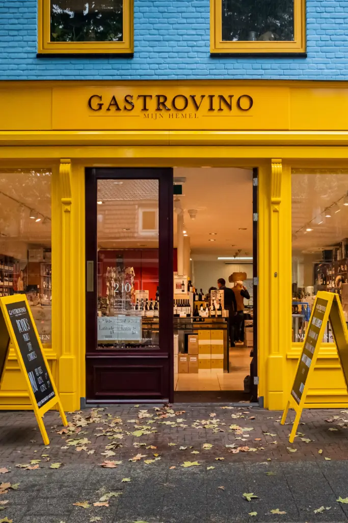 De gele gevel van Gastrovino Mijn Hemel aan de Gijsbrecht van Amstelstraat in Hilversum, met de deur open.